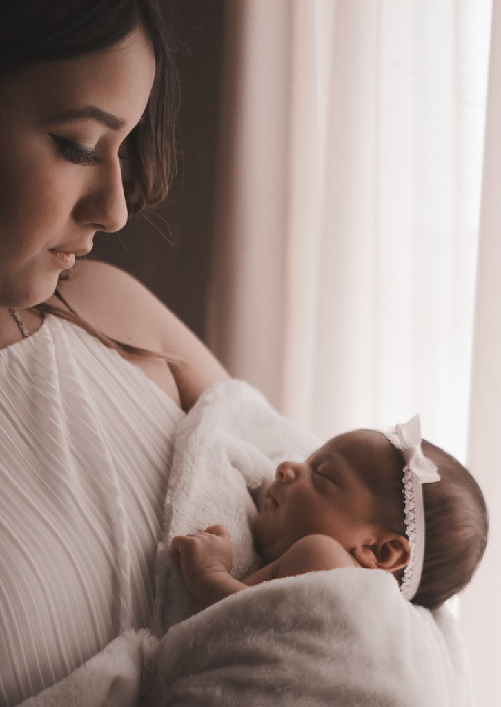 Tender moment of a mother holding her newborn child by a window, capturing love and warmth.